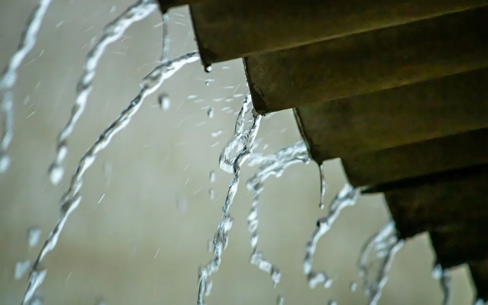Agua de lluvia cayendo en chorros desde el borde de un techo